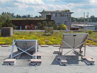 The measuring equipment on the test roof: In the foreground, Modules 1 and 2 on the bitumen membrane and in the background Module 3 on the green roof. The weather station for measuring air temperature can be seen beside Module 3. Measuring equipment on the test roof